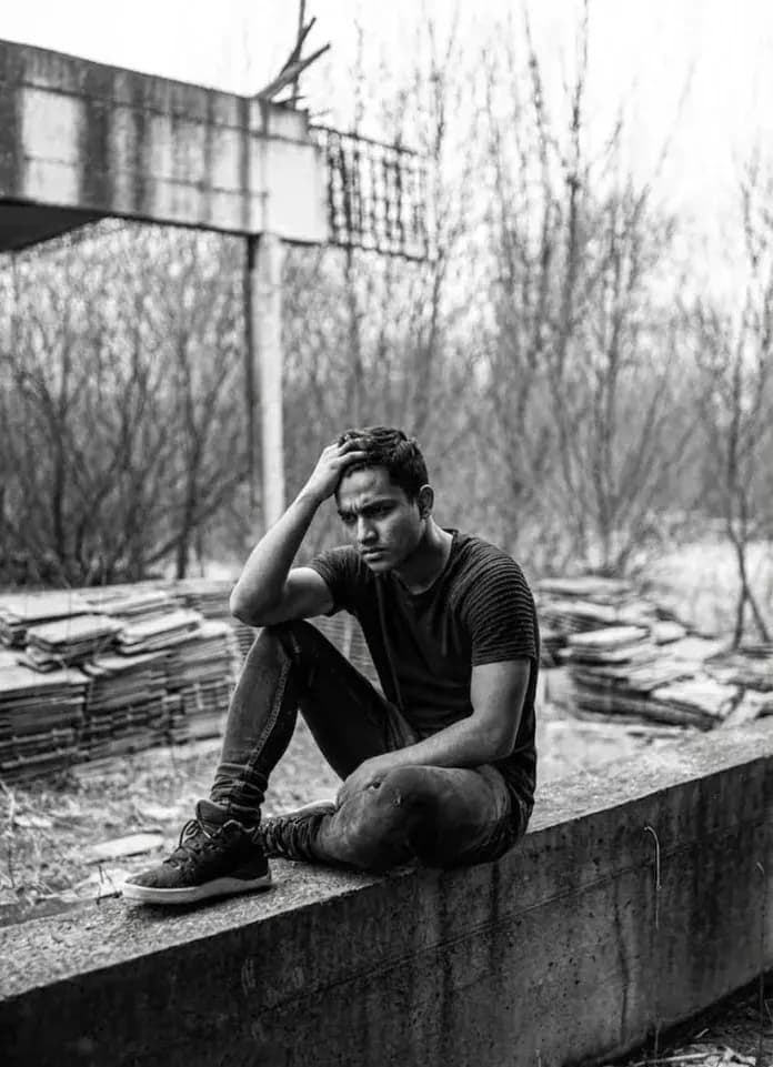 Young man sitting outdoors, looking stressed and holding his head